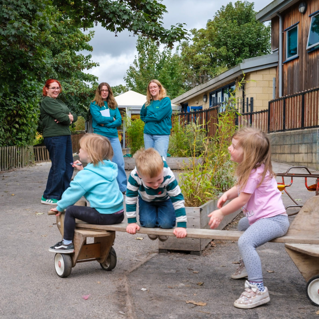3 children playing on a driveable toy with Rise staff watching in the background